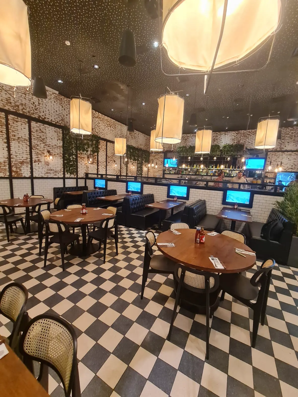 חלל מסעדה עם גופי תאורה תלויים בצורת גליל בד ורצפת שחמט